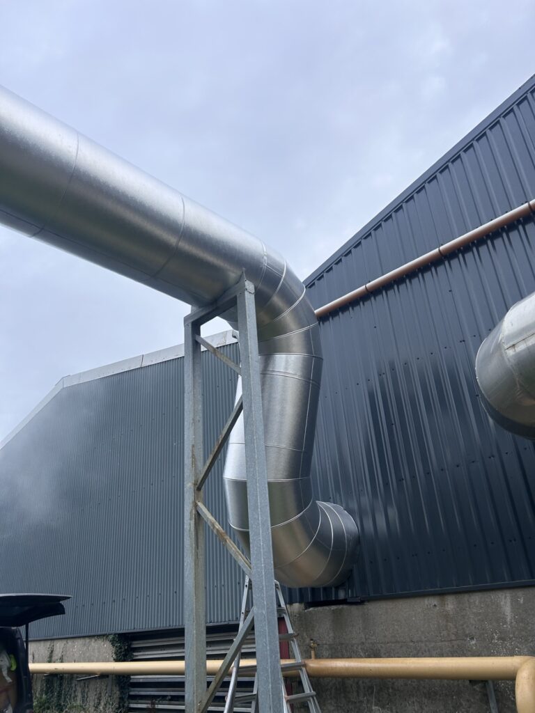 Aluminium-clad flue bend and vertical drop beside an industrial building, Co. Meath