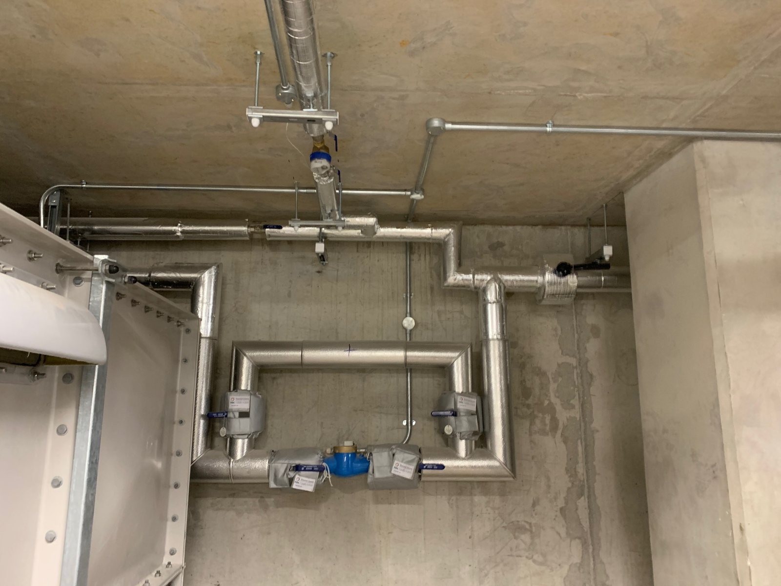 Insulated wall-mounted pipework with branches around a service connection.