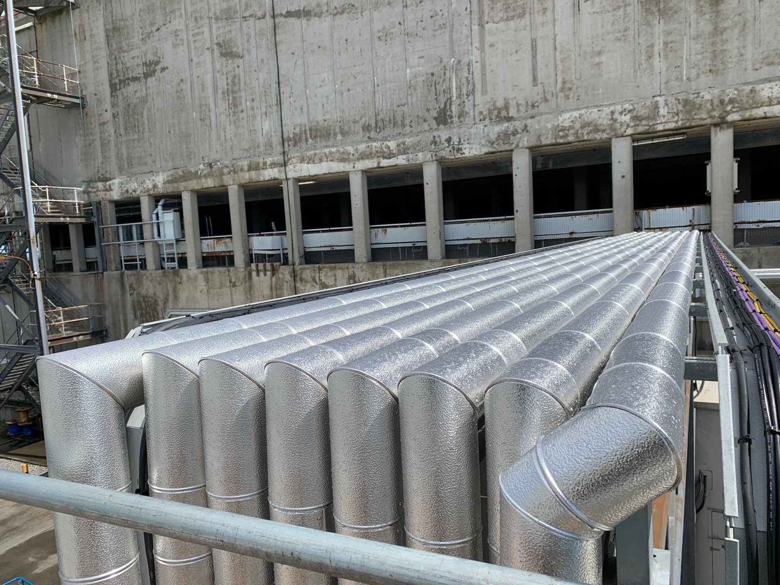 A bank of parallel insulated pipes finished with formed metal cladding.
