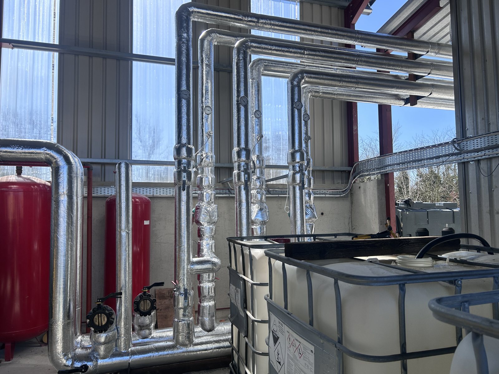 Metal-clad insulation on industrial plant-room pipework, bends and risers.