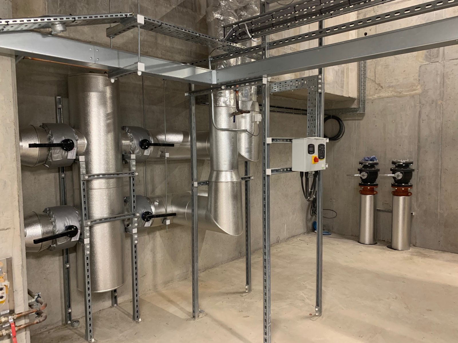 Detail of insulated pipework, formed bends and branches along a plant-room wall.