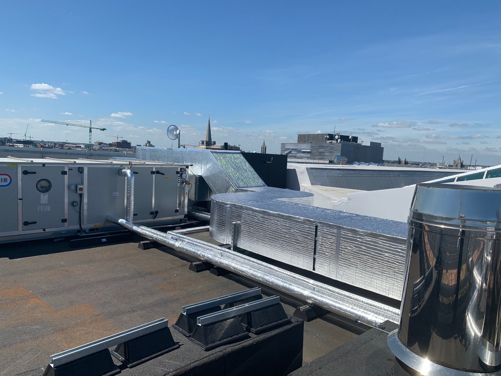 Clad ductwork and branch connections alongside rooftop air-handling equipment.