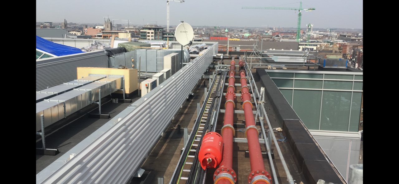 Before insulation: exposed red pipe runs on a roof-level services route.