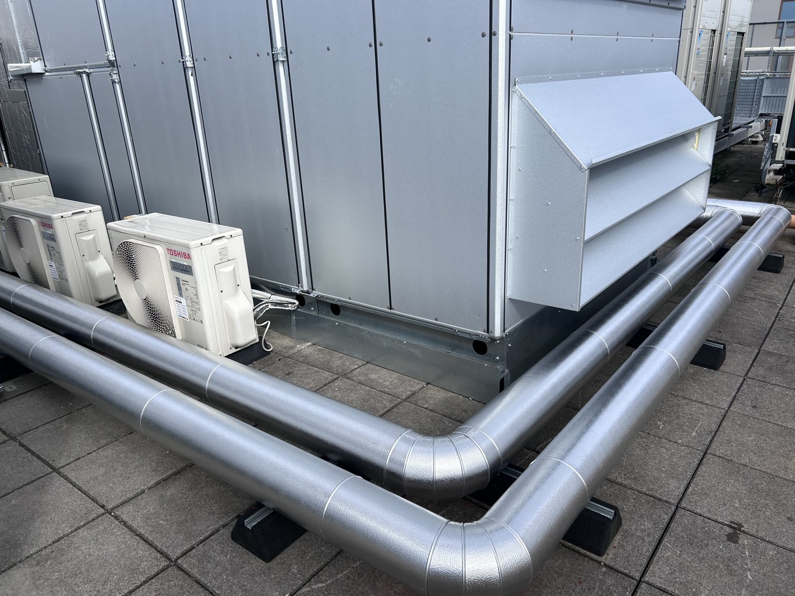 Protective cladding on roof-level pipe bends beside mechanical equipment.